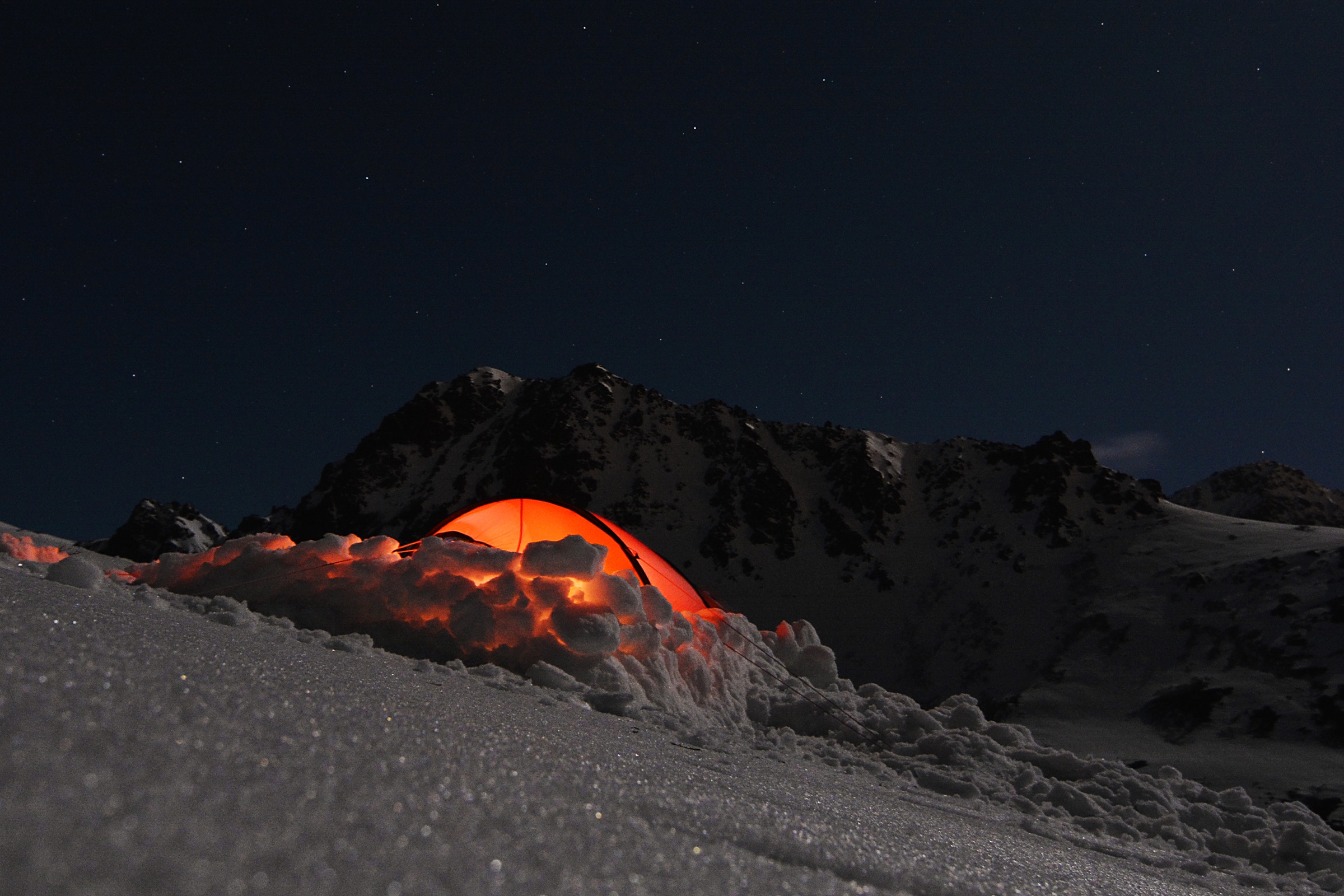 A tent glowing at night at a backcountry campsite