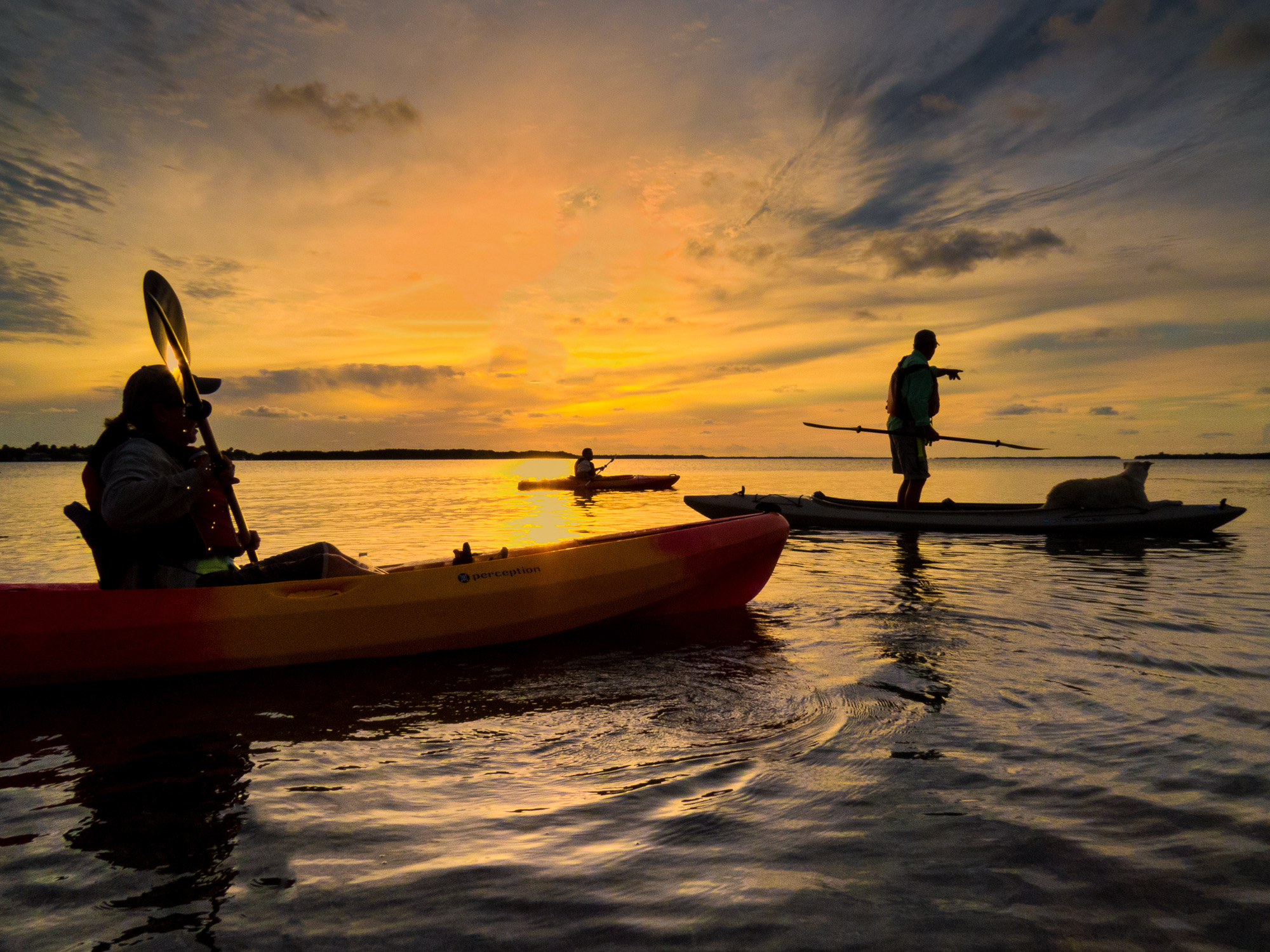 Three kayakers silhouetted against a glowing orange and pink sunset sky on calm Florida waters in the Great White Heron National Wildlife Refuge