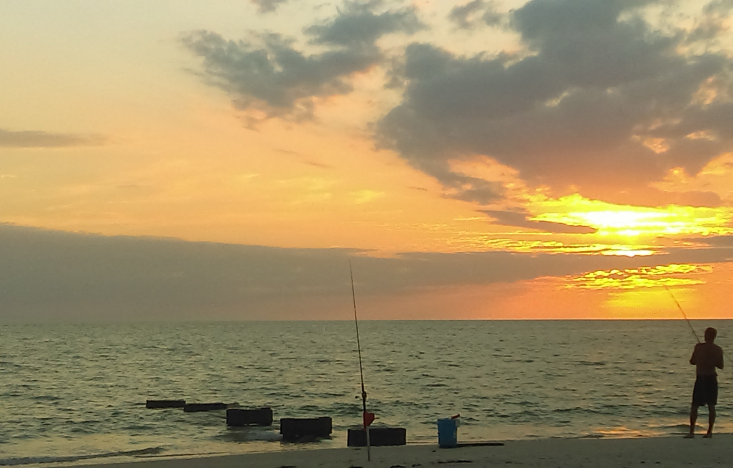 An angler surf fishing at sunset on a Naples, Florida beach