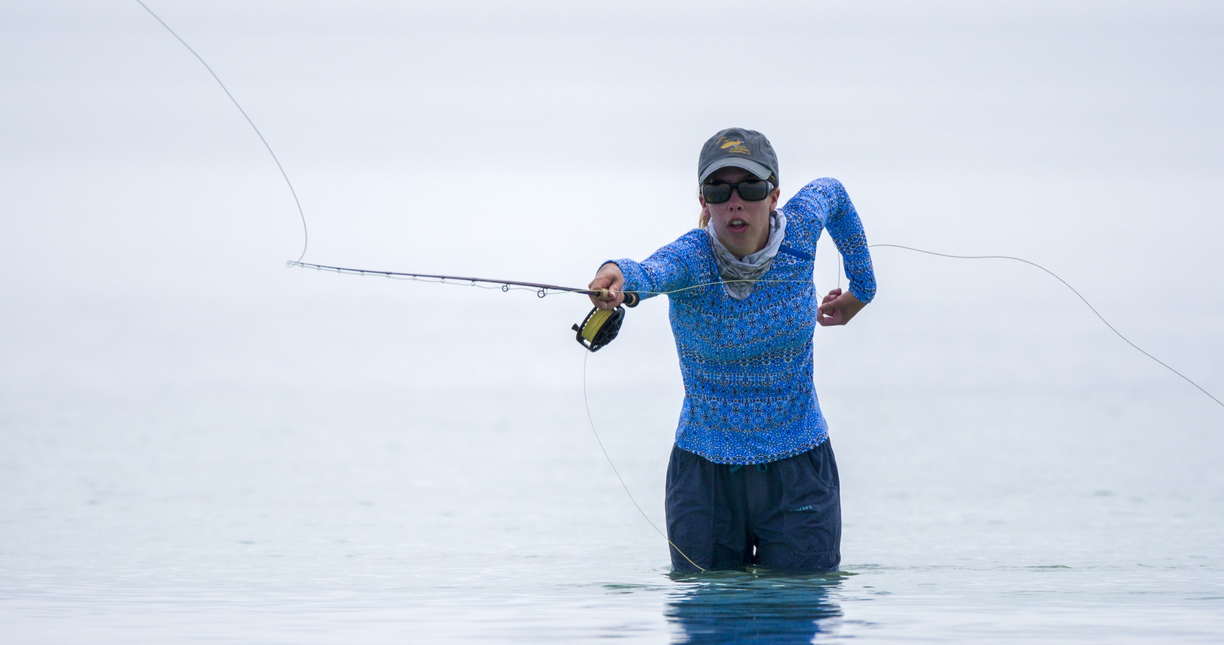 An angler stands in shallow, sunlit waters of the Florida Keys National Marine Sanctuary, casting a fly rod across the crystal-clear flats