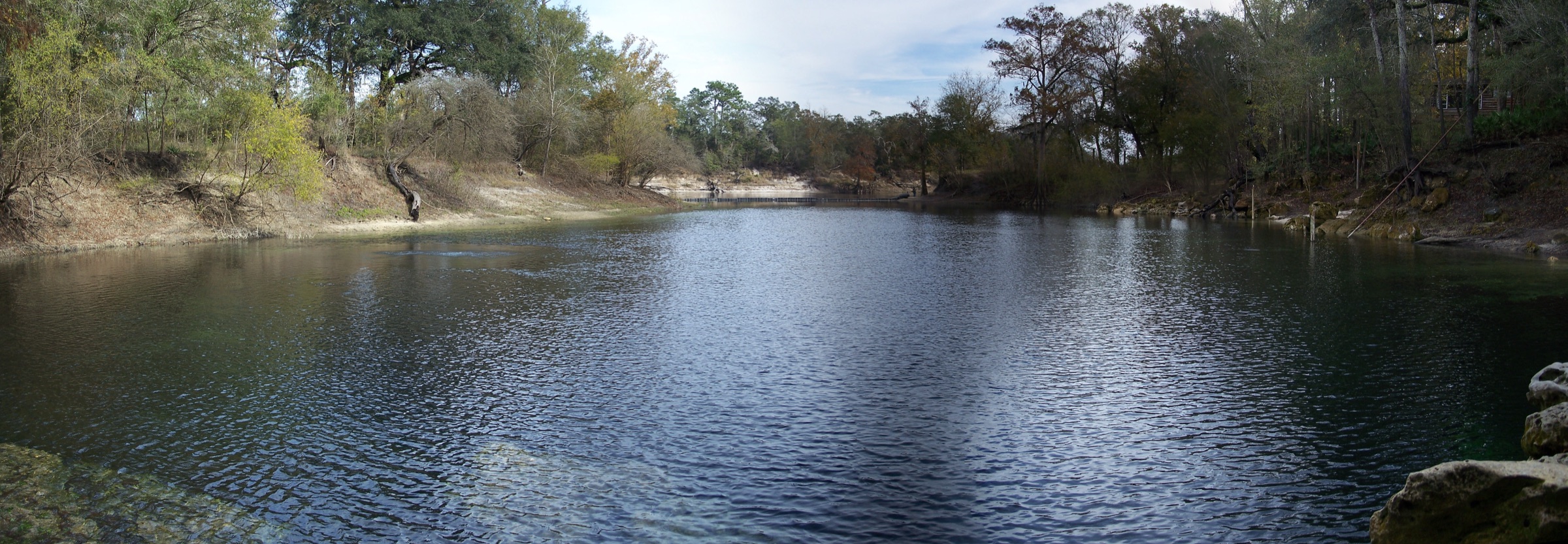 Panoramic view of the clear blue-green spring pool at Troy Springs State Park in north Florida, surrounded by limestone banks and subtropical vegetation