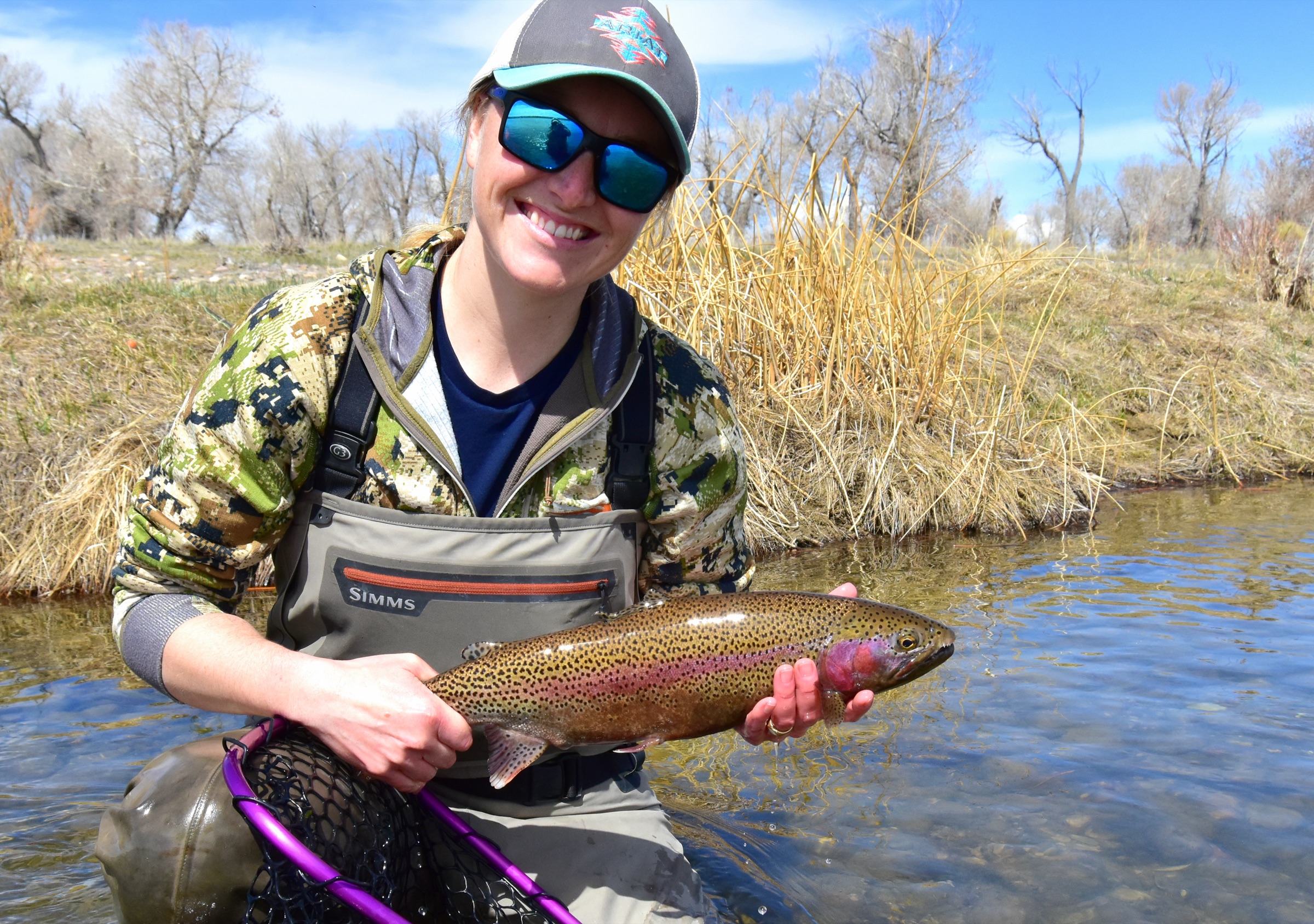 An angler in waders stands mid-stream in clear water, casting a fly rod while fly fishing for trout at Seedskadee National Wildlife Refuge