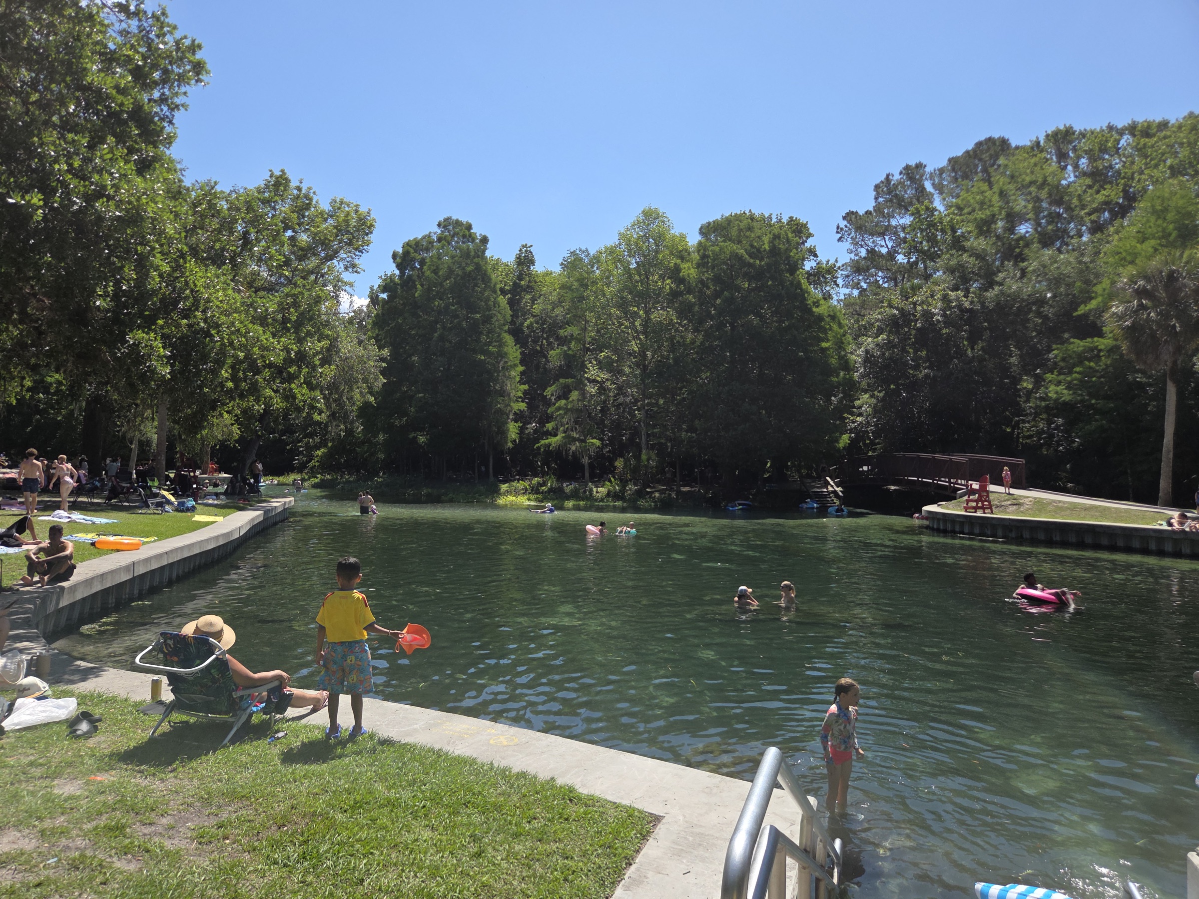 Clear green spring-fed swimming basin at Kelly Park with people tubing and swimming, surrounded by Florida forest