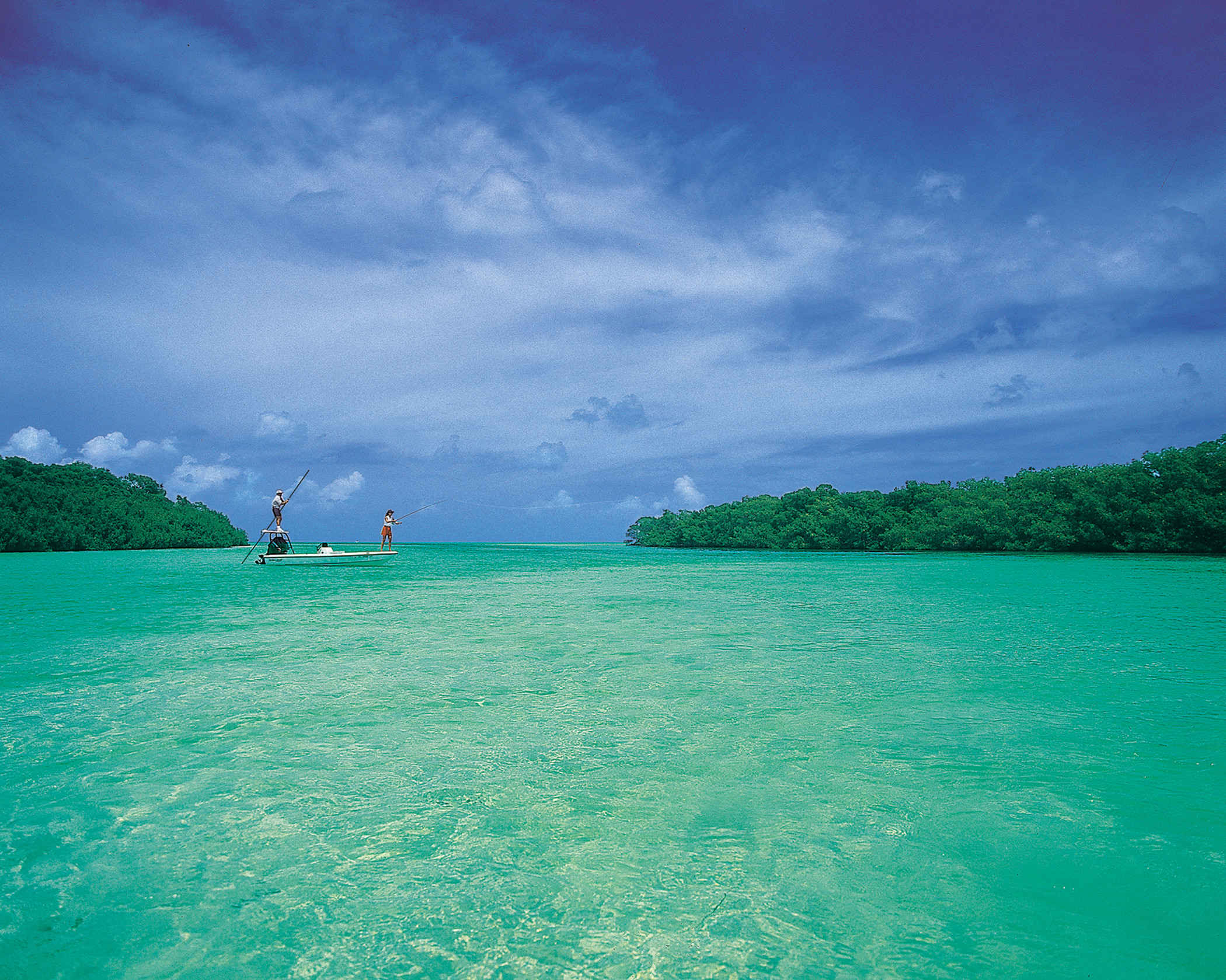 Two anglers flats fishing in shallow, clear aquamarine water near Islamorada, Florida Keys, with mangrove islands in the background